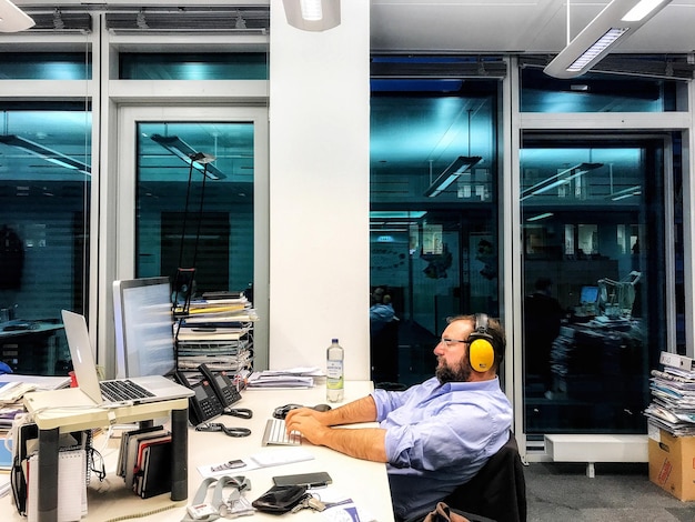 Photo side view of businessman wearing headphones while working in office