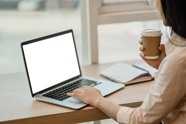 Side view of businesswoman drinking coffee and using laptop on wooden desk