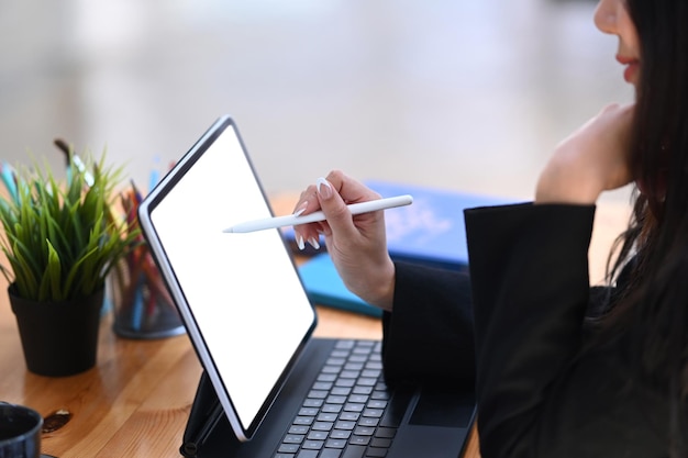 사무실에 앉아 있는 동안 그녀의 작업을 계획하는 디지털 태블릿을 사용하는 여성 사업가의 측면 보기.