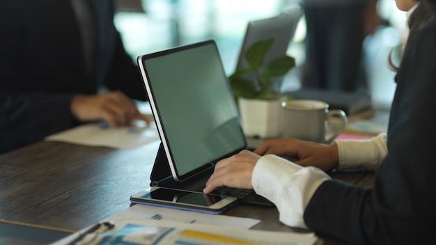 Side view of businesswoman working with tablet and paperwork while meeting with coworker