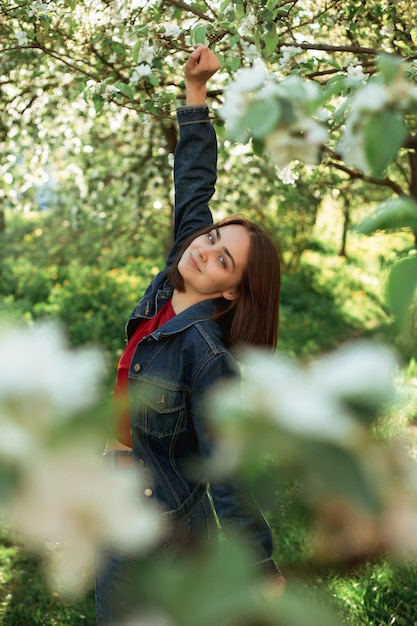 Side view of carefree woman in denim jacket standing with outstretched arms