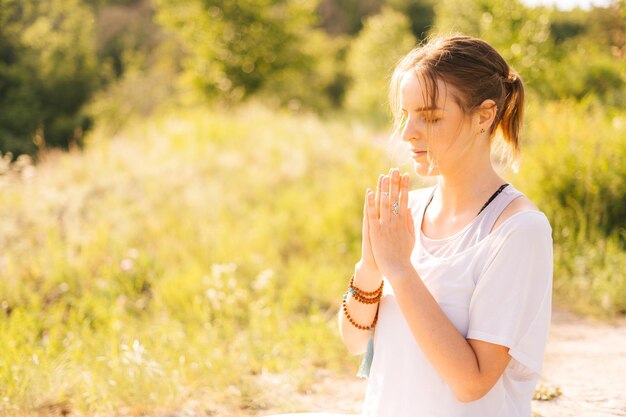 Side view of carefree young woman meditating in lotus position with closed eyes and holding hand in namaste yoga pose Lady prayer meditating in Namaste mudra Concept of practicing yoga alone outdoor