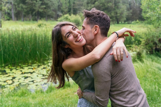 Side view of caucasian couple in love laughing and hugging. Horizontal view of couple hugging and kissing with love outdoors in nature background. People and travel concept.