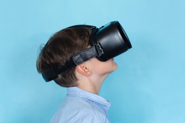 Side view of caucasian elementary schoolboy wearing vr glasses against blue background