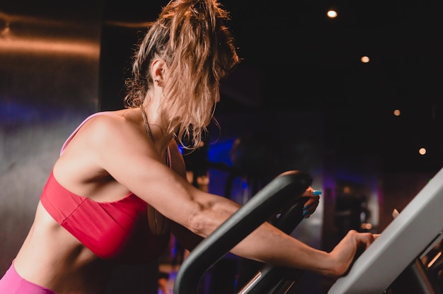 Vista laterale donna caucasica su trainer ellittico in palestra allenamento cardio