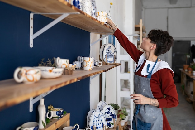 Side view of ceramics studio owner arranges a showcase with finished products for sale