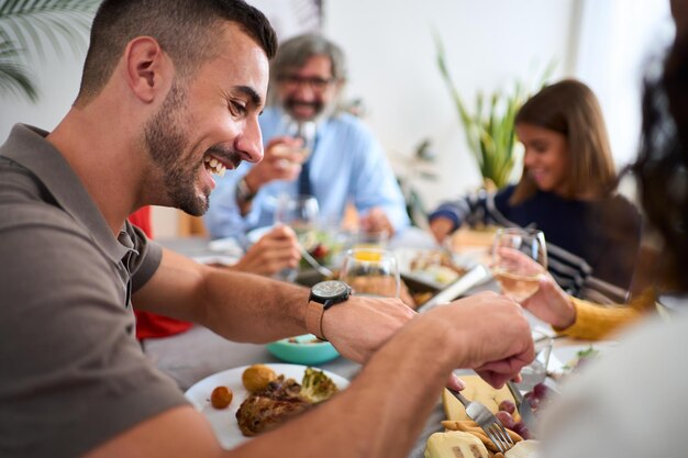 写真 家族と一緒にテーブルに座って食べている陽気な白人男性が背景に焦点を当てていない