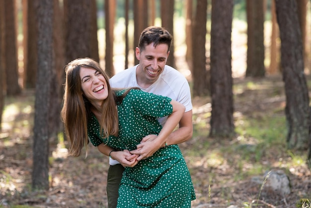 Side view of cheerful couple tickling each other in the forest. Horizontal view of young couple hiking on holidays in nature. Countryside travel and people concept.