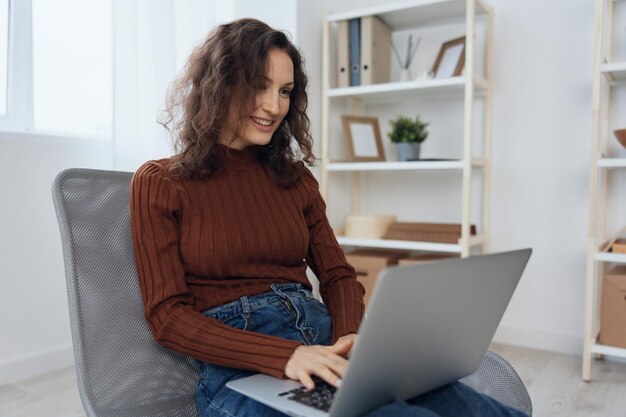 Side view of cheerful smiling happy curly beautiful lady enjoy\
online work using laptop doing nft design project loves her job\
sitting in chair at home modern profession and remote job