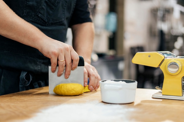 Photo side view of chef with apron slicing pasta dough