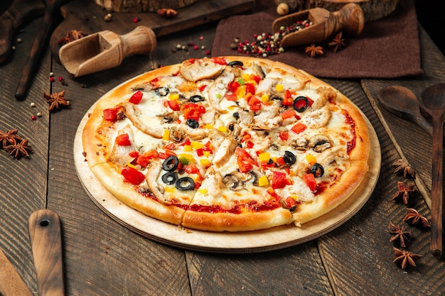 Side view on chicken pizza with mushrooms and vegetables on the\
wooden table