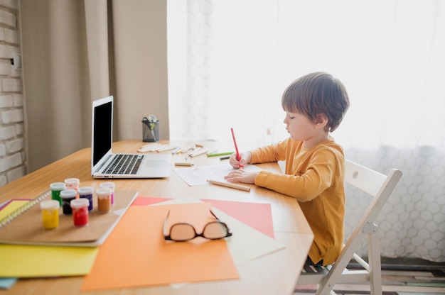 Vista laterale del bambino che impara dal computer portatile mentre a casa