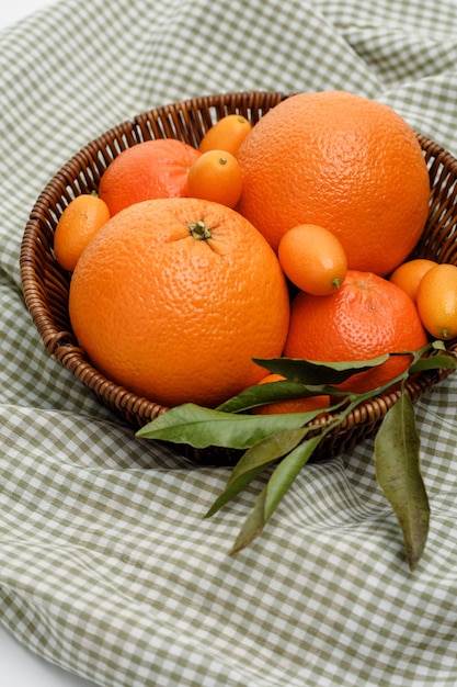 Vista laterale di agrumi come mandarino arancione e kumquat in cestino su sfondo di stoffa a quadri