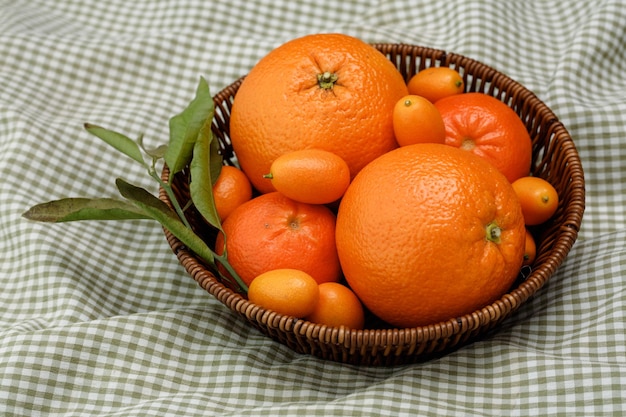 Side view of citrus fruits as orange tangerine and kumquat in basket on plaid cloth background