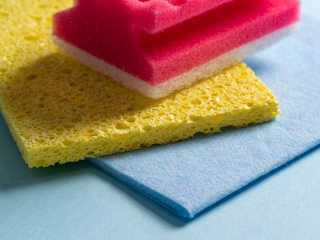 Side view of cleaning sponges of different colors and sizes laid out on a blue background. Home cleaning products