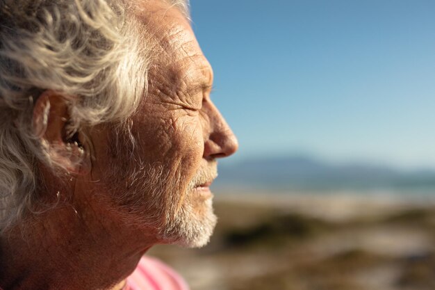 Вид сбоку крупным планом пожилого кавказца на пляже на солнце, улыбающегося с закрытыми глазами на фоне голубого неба