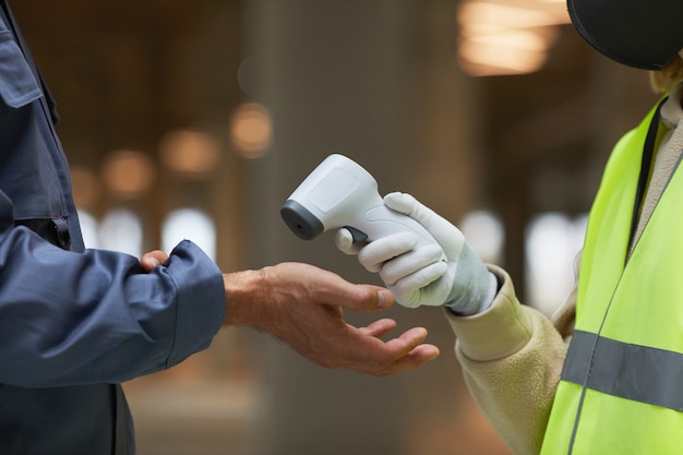 Side view close up of supervisor measuring temperature of workers with contactless thermometer pointing at hands, 