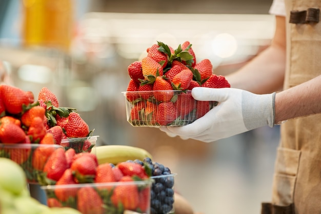 Side view close up of unrecognizable man holding box of delicious fresh strawberries at fruit and vegetable stand in farmers market