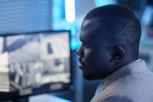 Side view closeup portrait of black man looking at surveillance camera feed in monitoring and securi