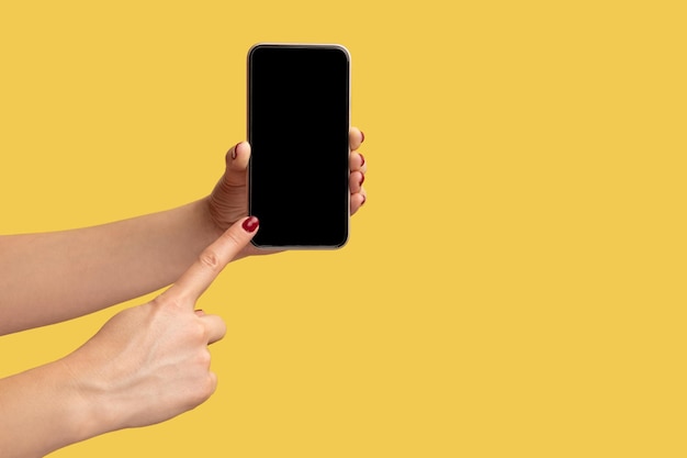 Side view closeup of woman hand holding and showing smart phone and pointing at empty display