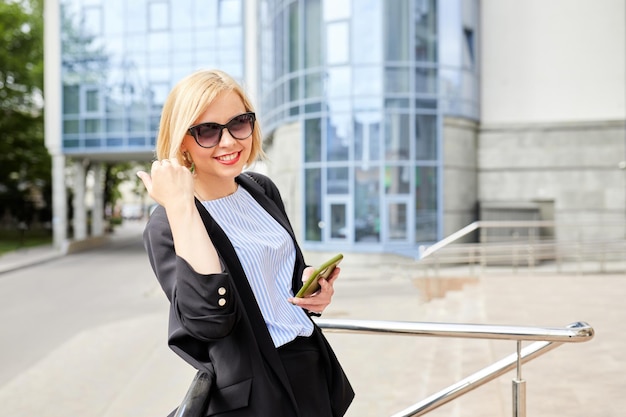 Side view of concentrated woman in stylish outfit text messaging on mobile phone while walking along near contemporary building