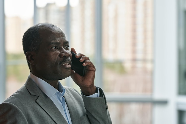 Side view of confident mature African American broker with mobile phone