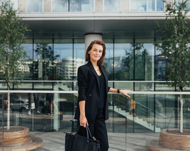 オフィスビルの向こうに立っているバッグを持った自信のある中年女性ビジネスマンのサイドビュー