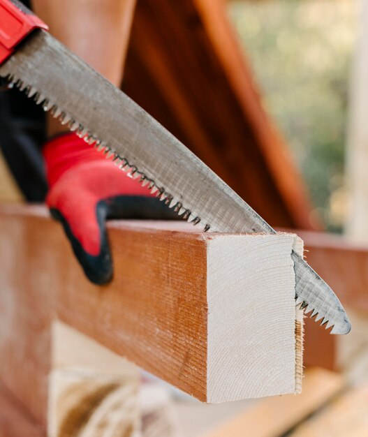 Photo side view of construction worker cutting piece of wood with saw