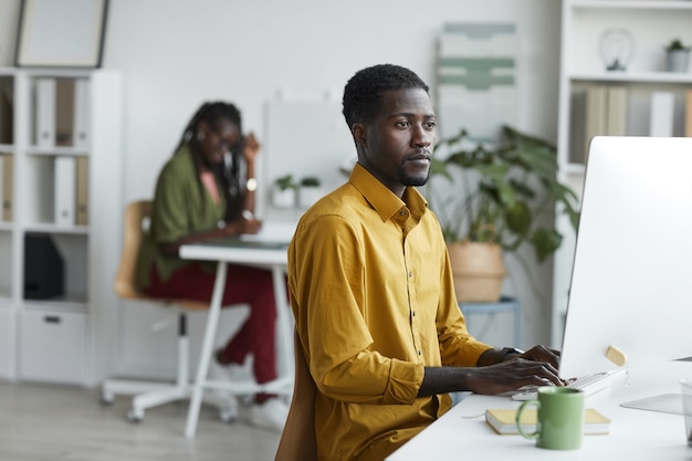 흰색 사무실 인테리어, 복사 공간에 책상에서 작업하는 동안 컴퓨터를 사용하는 현대 아프리카 계 미국인 남자의 측면보기