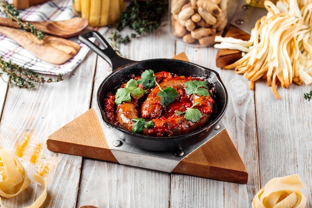 Side view on cooked large sausage in tomato sauce in castiron pan