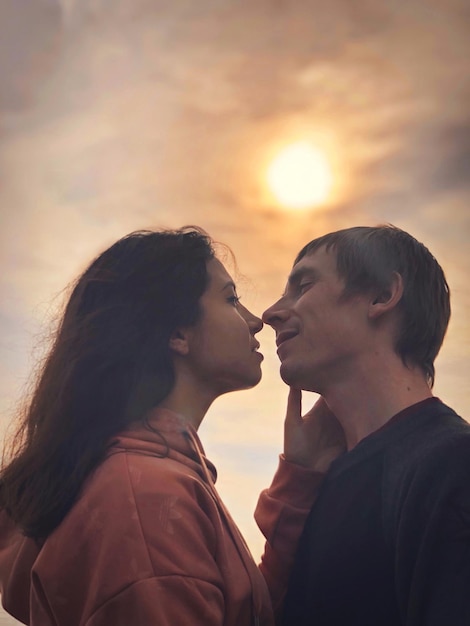 Side view of couple face to face against sky during sunset