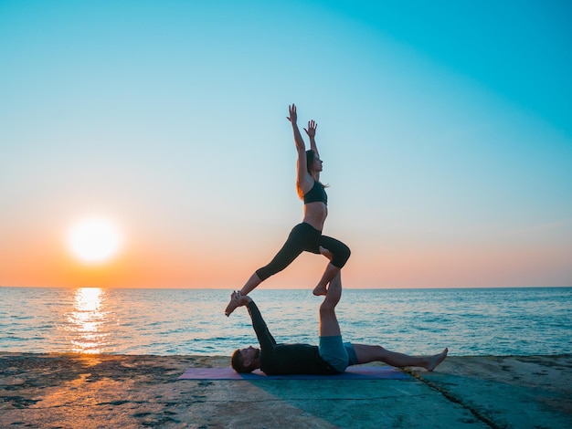 Photo side view of couple practicing yoga on pier by sea against sky during sunset