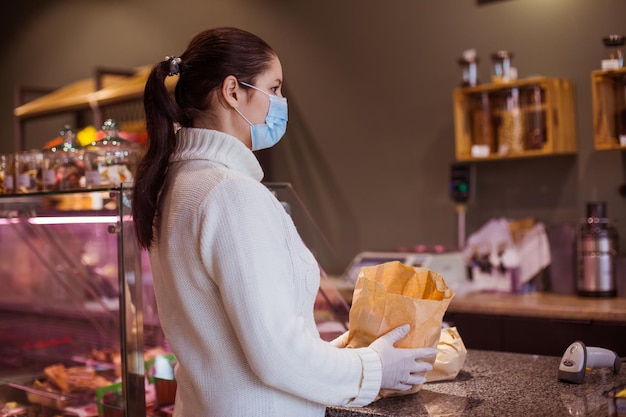 Side view customer at the small grocery shop Young woman near counter holding paper bag Supporting local business while pandemic concept