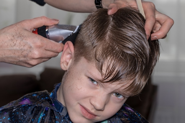 Side view of cute little boy getting haircut by hairdresser at the barbershop.