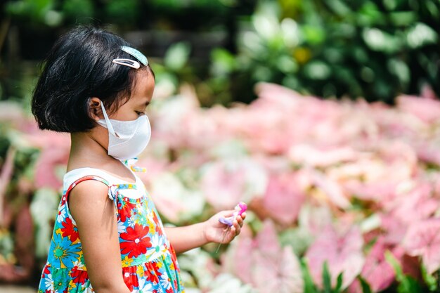 Side view Cute small girl wearing protective face mask standing against pink plants at tree shop