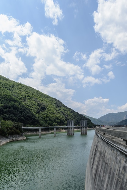 Side view of a dam with a mountain forest & clouds