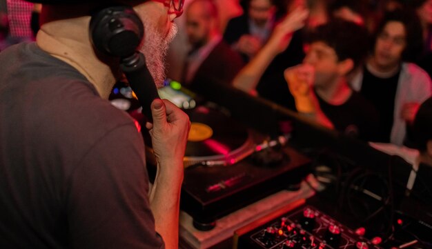 Photo side view of a deejay holding an earpiece while playing in the disco