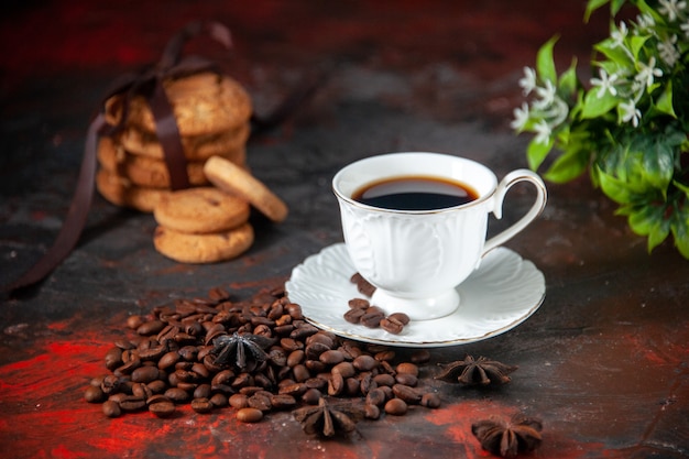 Vista laterale di un delizioso caffè in una tazza bianca e fagioli tostati impilati fiori di biscotti su uno sfondo di colore misto con spazio libero