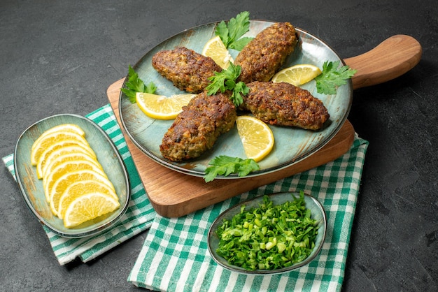 Side view of delicious cutlets served with lemon and green on wooden cutting board on yellow stripped towel on black background