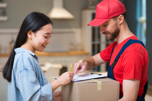 Side view of delivery man showing woman where to sign to receive order