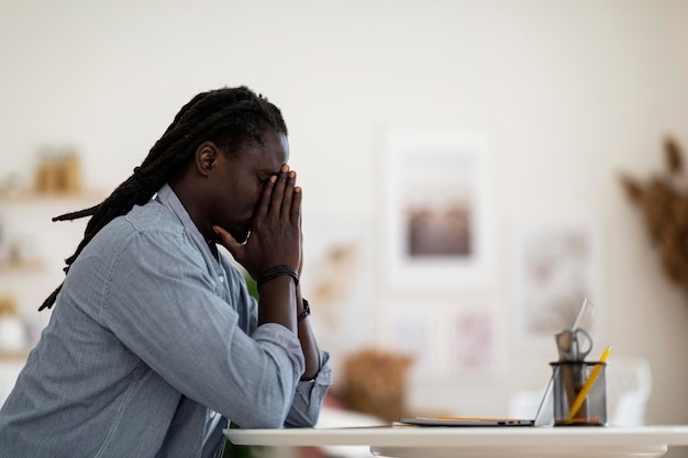 side view of depressed african american man sitting at desk with laptop