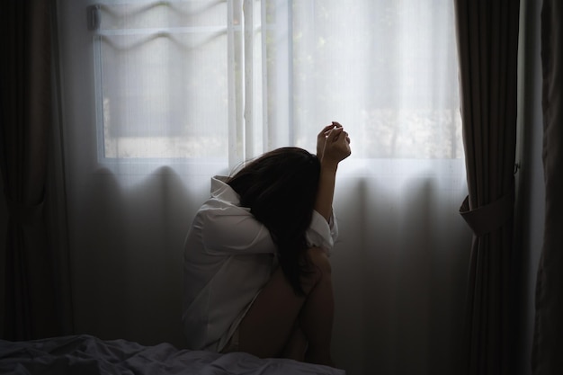 家の窓のそばに座っている落ち込んだ女性の横の景色