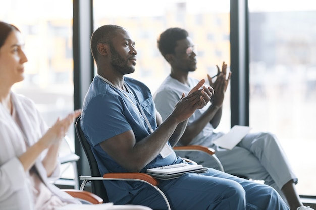 Side view at diverse group of doctors applauding during medical conference or seminar , copy space