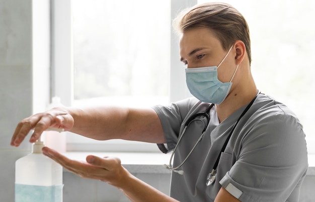 Foto vista laterale del medico con mascherina medica utilizzando disinfettante per le mani