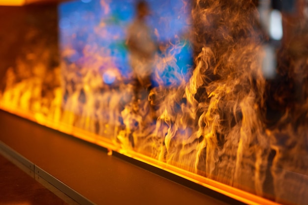 Вид сбоку на электрический камин с искусственным искрящимся пламенем, декором для интерьера, синим и оранжевым пламенем с подвесным креслом-качалкой в отражении