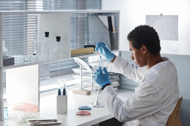 Photo side view ethnic young man doing tests at workstation in modern laboratory