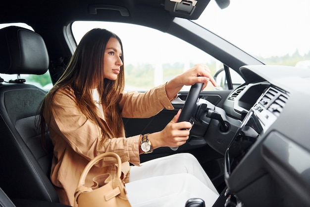 Side view of fashionable beautiful young woman that is inside her modern automobile