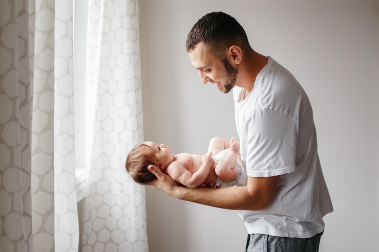 Photo side view of father carrying baby daughter against wall at home