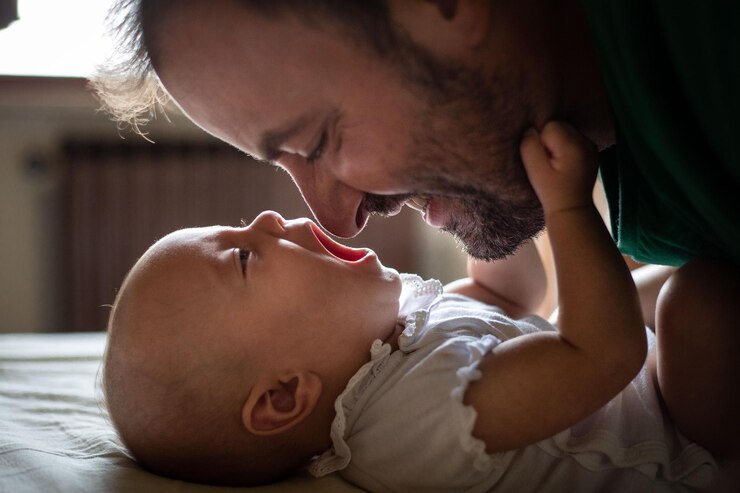 Photo side view of father face watching his newborn baby in white top laying on the bed