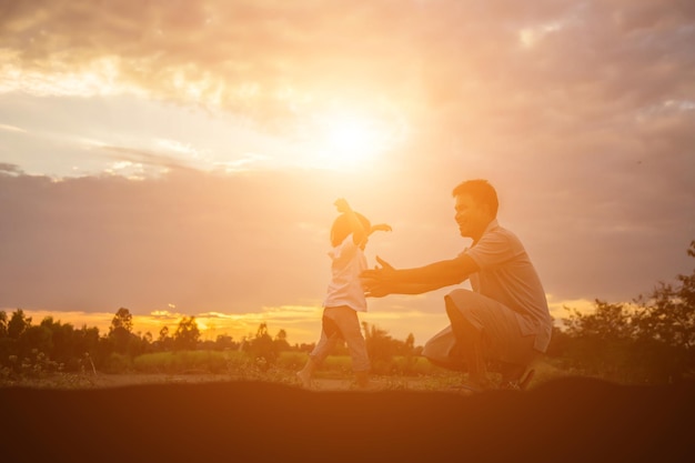 Side view of father gesturing towards daughter on land against sky during sunset